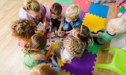 Eine Gruppe Kinder sitzt mit einer Erzieherin im Kreis und spielt Karten. Eine Gruppe Kinder sitzt mit einer Erzieherin im Kreis und spielt Karten.