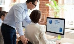 Bild zeigt einen Mann, der einer Frau an einem Computer etwas erkärt