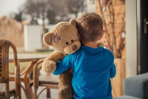 Hier ist ein Bild von einem Kind mit einem Teddybären zu sehen.