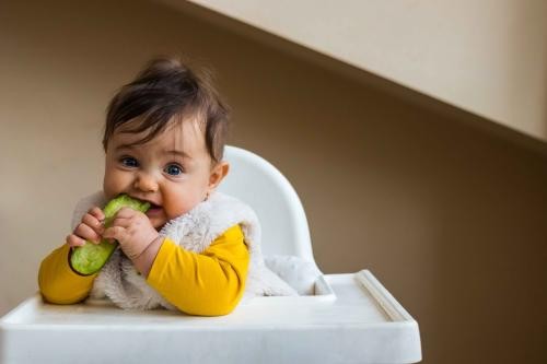 Hier ist ein Kleinkind zu sehen: Das Kleinkind hält Gemüse in der Hand.