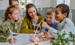Auf dem Bild sind junge Schülerinnen und Schüler mit ihrer Lehrerin zu sehen. Sie Sie schauen sich ein Modell eines Windrades an. Auf dem Bild sind junge Schülerinnen und Schüler mit ihrer Lehrerin zu sehen. Sie Sie schauen sich ein Modell eines Windrades an.