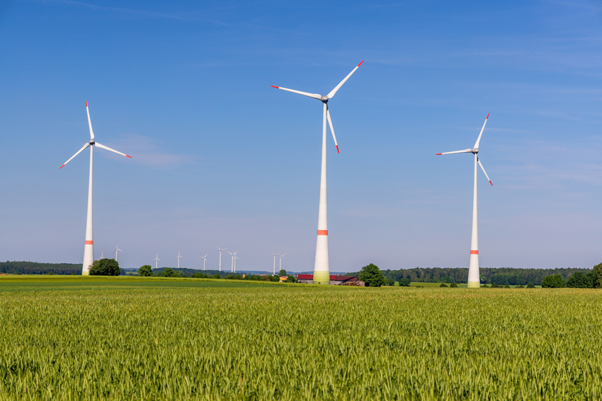 hier ist ein Landschaftsbild zu sehen: mit grüner Wiese, drei Windräder und wolkenlosem blauen Himmel
